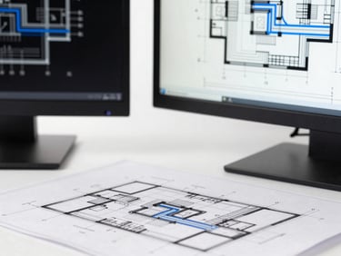 Tight macro shot of architectural blueprints next to a high-performance monitor displaying vector lines, high-contrast monochrome with electric blue accents.