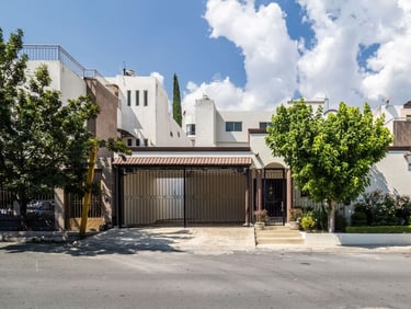 Casa residencial moderna de color blanco con entrada cerrada y árboles verdes y cielo azul