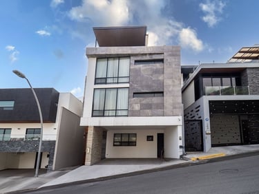 Fachada de moderna casa de tres niveles con acabados en piedra gris, amplios ventanales y cochera te