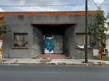 Un edificio urbano con paredes de estuco gris, molduras naranjas y grafiti en la entrada con reja.