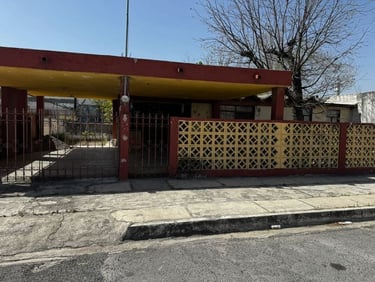 Casa residencial con cochera roja y amarilla, muro decorativo de bloques de hormigón y verjas
