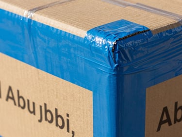 A close-up of heavy-duty cardboard box corners double-wrapped in thick protective blue stretch film, labeled clearly in bright Abu Dhabi daylight.