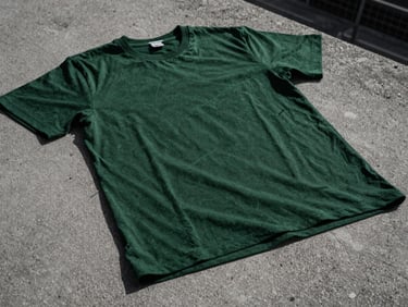 Close-up of a dark green t-shirt with a subtle, abstract weather pattern graphic, on a textured concrete surface, overcast natural daylight, high-contrast desaturated tones.