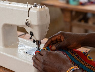 Close-up of hands guiding a colorful fabric through a mechanical sewing machine, soft natural side lighting.