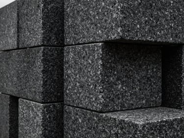 Tactile close-up of heavy dark granite blocks stacked in geometric alignment, natural overcast light, sharp textures.