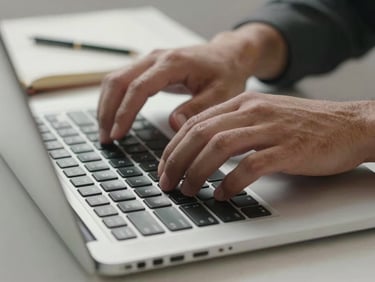 Tight close-up of hands typing on a laptop keyboard, notebook with handwritten notes beside it, clean studio lighting from the left, shallow depth of field on the keys