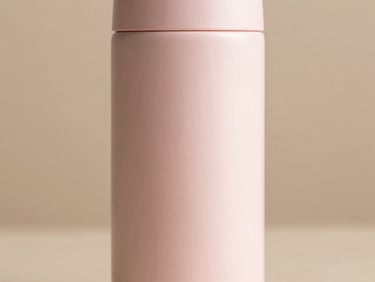 Close-up of a matte pastel pink thermos with clean typography on a warm beige background, soft side lighting