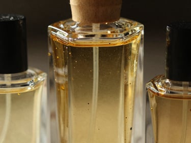 Macro close-up of thick, geometric glass perfume bottles filled with gold-flecked attar oil, catching dramatic light against a dark background.