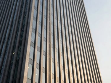 Dramatic low-angle architectural shot of a modern corporate skyscraper facade in Hyderabad, sharp golden-hour highlights reflecting off glass and steel panels, clean geometric lines