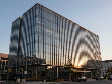 Wide environmental shot of a modern glass-fronted corporate headquarters building, sharp golden-hour highlights