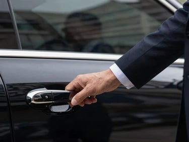 Close-up of a professional driver in a tailored dark suit opening the door of a pristine black executive car, focus on the hand and the polished door handle, elegant composition.