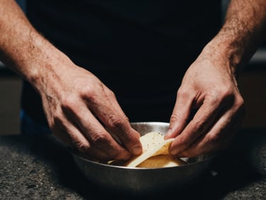 Moody close-up of hands preparing a classic dish in a dimly lit kitchen, warm light on food, dark background, 35mm lens