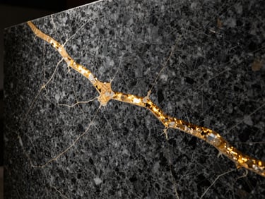 Close-up of a raw dark granite slab with golden quartz veins, dramatic architectural side lighting, sharp focus