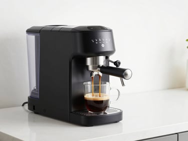 A sleek black single-serve espresso machine brewing coffee into a glass mug, clean kitchen counter, natural daylight