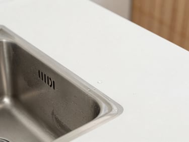 Macro shot of an integrated stainless steel sink in a clinical white countertop, jointless construction, water droplet, bright natural daylight