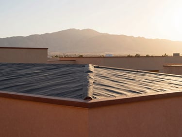 Textured detail of a dark torch-down roofing membrane on a flat commercial roof, mountain silhouette in background.