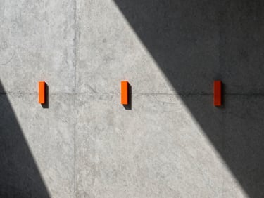 Raw concrete wall texture with sharp safety orange markers, high-contrast lighting casting strong geometric shadows.