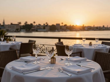 Close-up of an upscale restaurant table set on a private terrace overlooking the Nile at sunset, golden hour light, elegant crystal glassware, soft focus.