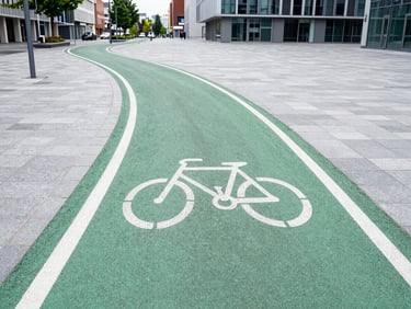 An urban bike lane made of green asphalt curving through a modern European city square, morning light