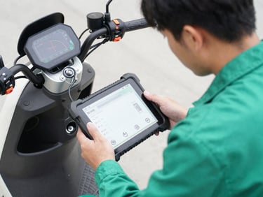 A mechanic using a digital diagnostic tablet connected to an electric scooter motor hub, focused technical setting, sharp focus
