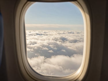 Serene window-seat view of clouds from an airplane, soft golden hour tones, shallow depth of field, warm editorial photography