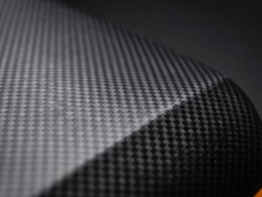 Extreme close-up macro of carbon fiber textured automotive vinyl wrap material on a dark surface, studio lighting emphasizing the woven diagonal pattern and depth, dark background