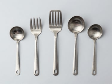 Industrial stainless steel kitchen utensils laid out on a clean gray background, top-down flat lay
