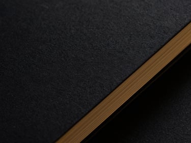 Dramatic close-up of textured black paper pages of a physical business guide, gold gilded edges, dark low-key lighting