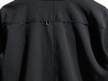 Inside view of a black garment, showing raw-edged seams and precise stitching, under cold industrial lighting, high contrast, 35mm film, sharp focus.
