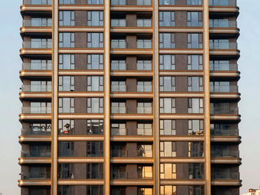 Modern luxury residential high-rise building with glass facade, golden-hour sunlight reflecting on premium materials, architectural symmetry.