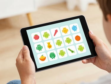 A child's hands holding an Android tablet displaying a colorful educational matching game, soft warm daylight, shallow depth of field