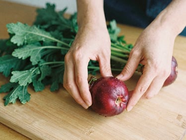 Hands carefully arranging fresh produce on a wooden board, soft natural light, shallow depth of field, rich crimson and forest green tones