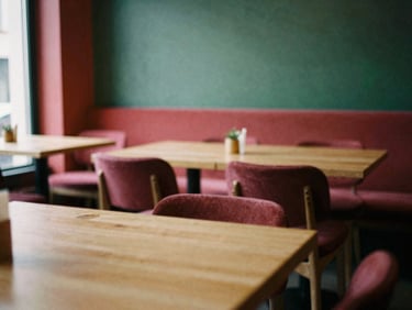 Cozy, scandinavian-style restaurant interior with warm lighting, empty tables, focus on natural wood and clean lines, soft daylight, rich crimson and forest green tones, shallow depth of field, 35mm film.