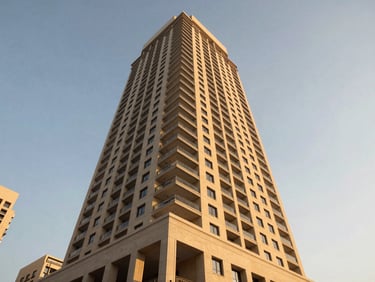 Environmental exterior shot of a mid-rise residential tower in Business Bay at golden hour, shot from street level looking upward, warm facade light against a clear sky, no people, architectural detail visible on the podium level