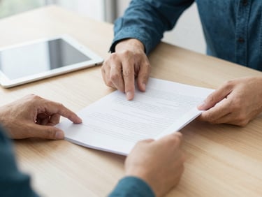 Close-up of professional hands organizing documents on a clean wooden table next to a tablet, bright natural lighting
