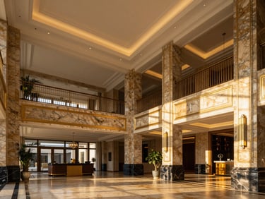 Wide-angle architectural photography of a sunlit luxury apartment lobby with double-height ceilings, marble pillars, and warm gold accents
