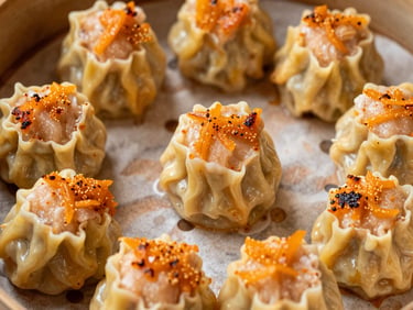 Top-down close-up of a large sharing platter with twelve pieces of dimsum, heavily torched orange mentai sauce covering every corner, rich and creamy