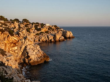 Ras Um Sid clifftop coastline in golden hour light, rocky shoreline dropping into deep blue water, a small resort terrace visible above the reef edge, no other buildings in frame