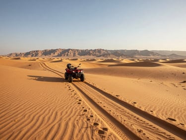 Wide desert landscape at the edge of Sharm El Sheikh, a quad bike trail cutting through golden sand toward distant mountains, late afternoon golden-hour light, clear sky above
