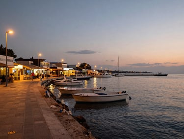 Naama Bay waterfront promenade at dusk, dive shops and restaurants visible along the seafront, boats moored in calm water, warm amber streetlight mixing with fading daylight