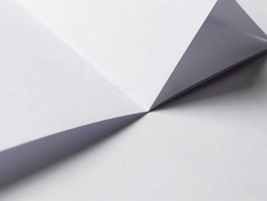 Macro close-up of sharp, folded white paper geometry casting crisp geometric shadows under hard directional daylight.