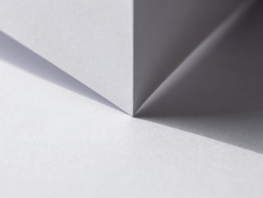 Macro photograph of white folded paper geometry, sharp diagonal shadows, hard directional daylight, minimalist composition, 50mm