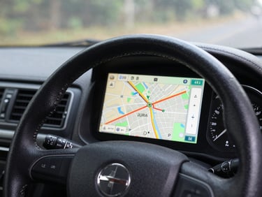 Close-up of a driver's dashboard GPS unit showing a Bangalore city route map, clean cab interior visible, steering wheel in foreground, morning light through windshield, functional and professional