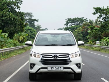 Wide highway shot of a clean Toyota Innova in motion on an Indian national highway, lush roadside greenery, bright overcast daylight, forward-facing dashboard perspective visible through windshield
