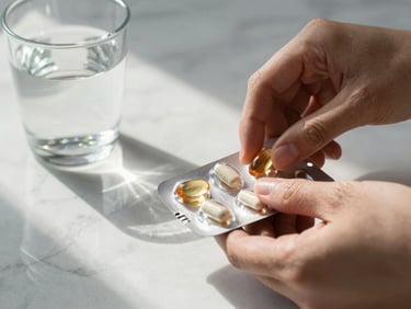 Close-up editorial of hands opening a vitamin capsule pack over a clean marble surface, morning light streaming from the left, a glass of water beside it, no faces