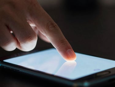 Extreme close-up of fingers interacting with a glowing mobile screen in a dark room, sharp cyan rim lighting reflecting on the glass.