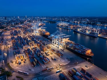 Professional industrial photography of a modern logistics port at blue hour, cargo ships and organized steel containers, sharp daylight tones, wide-angle aerial shot