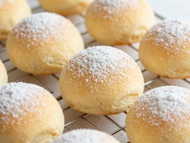 Close-up of a freshly baked pastry with a dusting of sugar on a cooling rack, golden light, soft yellow and cream tones.