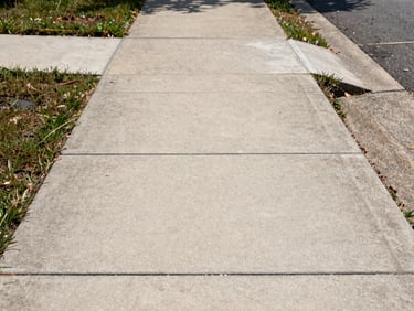 Straight-on shot of a finished concrete sidewalk in a Louisville residential neighborhood, clean expansion joints visible, flat even surface under morning daylight, sharp edges along both sides, no people