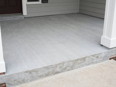Wide shot of a finished concrete porch at the front of a Louisville home, smooth broom-finish surface, clean step edges and corners, natural daylight, no people or furniture